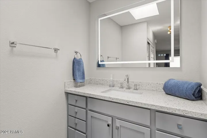 Primary vanity with quartz countertop, modern fixtures, and backlit mirror