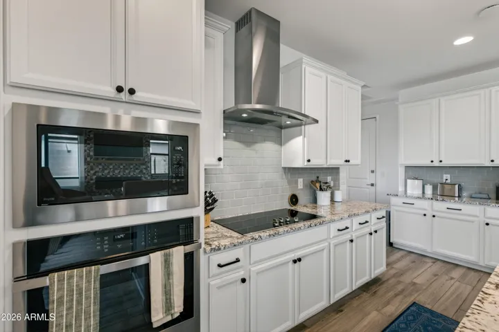 A bright, modern kitchen featuring white shaker cabinets, granite countertops, stainless steel appliances, and a clean subway tile backsplash.