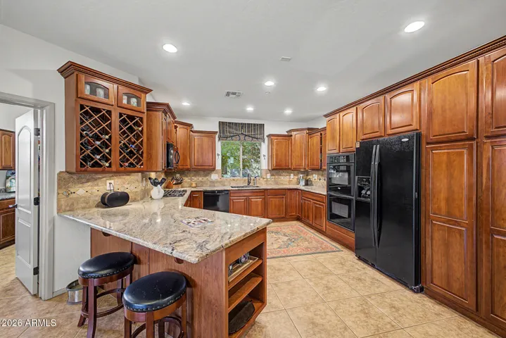 Granite countertops, custom cabinetry, recessed lighting, tile backsplash, sleek black appliances, and ample prep space make this kitchen both functional and beautiful.