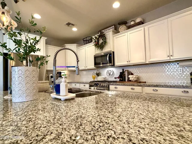 Stylish modern kitchen with staggered white cabinetry, a huge granite-topped island, and a beautifully tiled backsplash