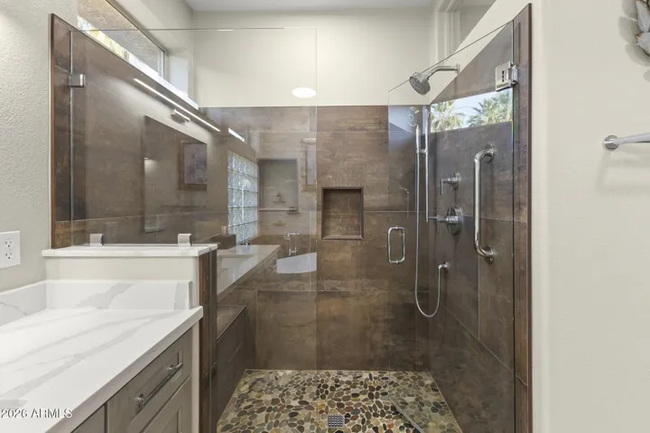 This walk in shower has beautiful glass doors, a seat, designer tile surrounds and a pebble style tile floor. There is a fixed shower head and a hand held. Niches provide convenience for toiletries.