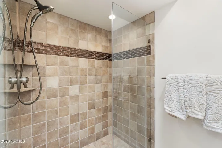 Elegant walk-in shower with floor-to-ceiling tile surround, decorative accent band, glass partition, and upgraded fixtures in this Scottsdale home.