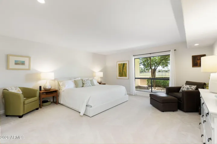 Oversized Scottsdale primary bedroom with sitting area, large window overlooking greenbelt views, plush carpeting, and bright natural light throughout.
