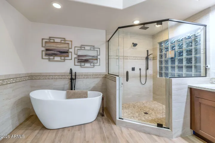 Remodeled primary bath features walk-in shower with floor to ceiling tile & soaker tub.