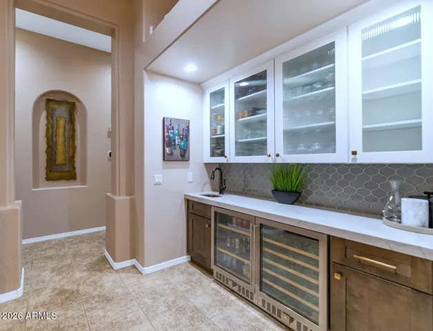 Wet bar area complete with copper sink, separate beverage & wine refrigerators, decorative backsplash, dual-tone cabinetry & obscure glass