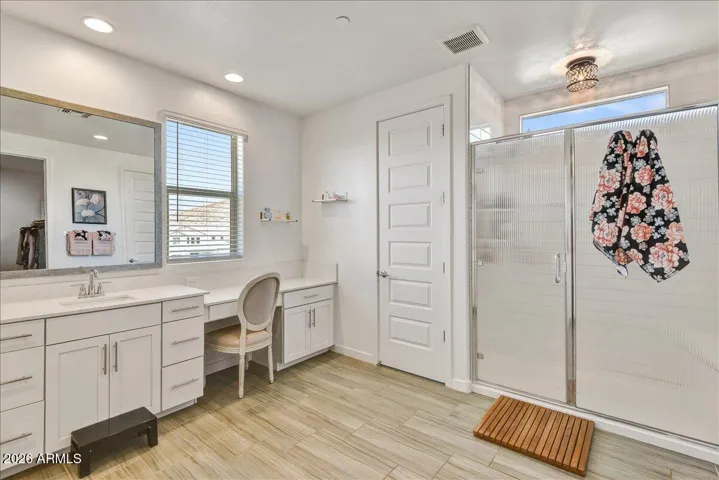 Another look at the primary bathroom reveals a spacious, bright layout. The modern white cabinetry, updated fixtures, and neutral flooring make it a highly functional, low-maintenance space.