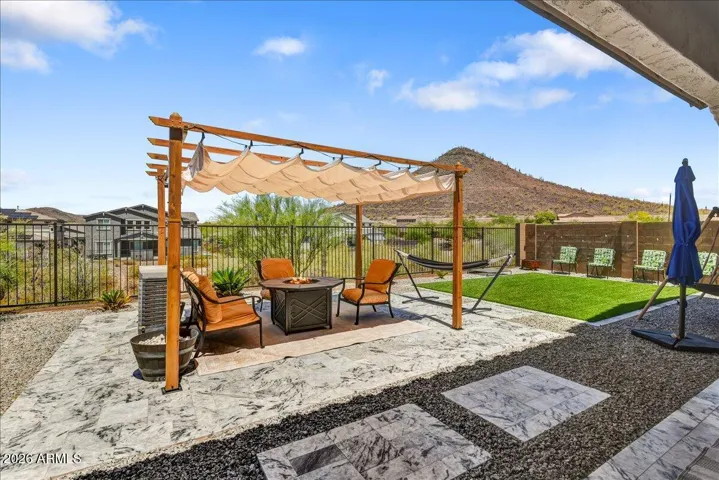 The beautifully landscaped backyard features an expansive layout complete with premium paver walkways, a dedicated open-air pergola section, and a pristine turf lawn. This low-maintenance oasis is highly functional and ideal for entertaining under the desert sky.