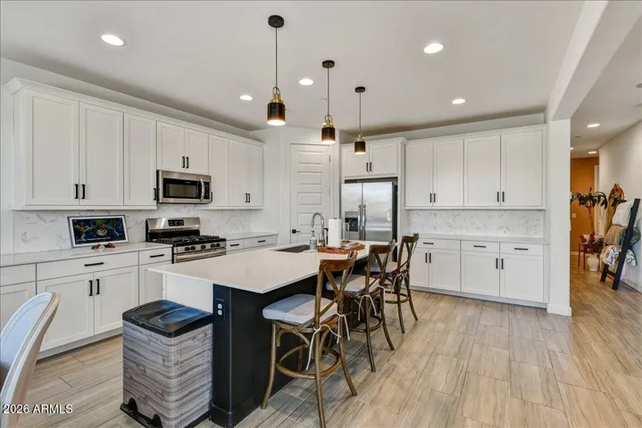 This gorgeous gourmet kitchen features a spacious central island, crisp white cabinetry with modern pull hardware, and elegant pendant lighting. Complete with premium countertops, a stylish tile backsplash, and stainless steel appliances, it is as functional as it is beautiful.