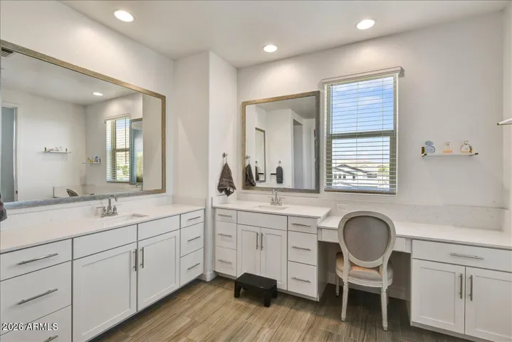 The spa-like primary bathroom boasts an extended, crisp white double vanity with plenty of cabinet space and a dedicated makeup/dressing station. A large wall-to-wall mirror and bright lighting fixtures create an exceptionally clean and elegant atmosphere.