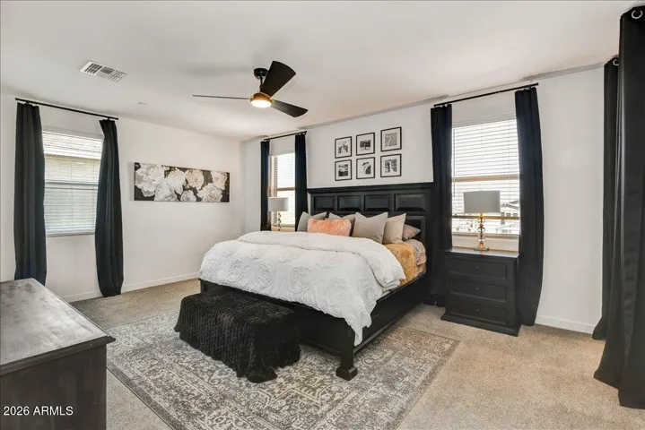 This expansive upstairs primary suite features a generous footprint designed for relaxation. With a cooling ceiling fan, large windows welcoming plenty of natural light, and a neutral palette, the room offers a peaceful retreat with ample space for a king-size bed and full matching furniture suite.