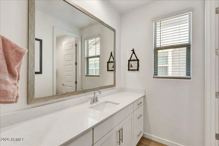 A beautifully lit upstairs bathroom featuring an extended white vanity with excellent cabinetry storage, a large mirror, and modern light fixtures. A well-placed window keeps the space feeling bright, open, and airy.