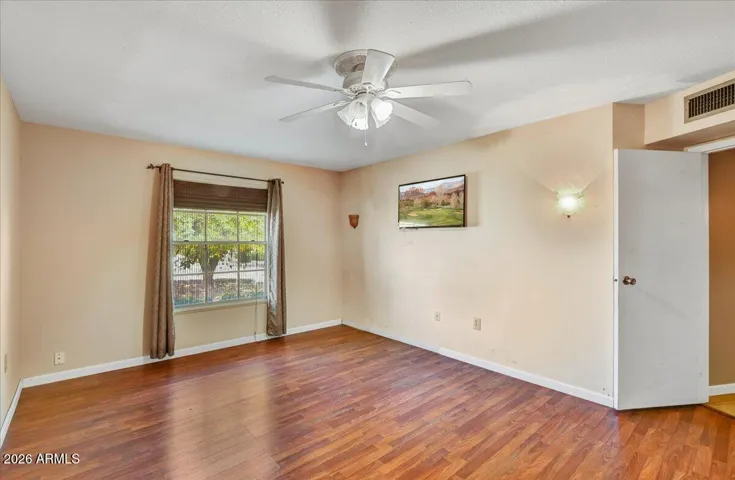 Well-sized additional bedroom featuring a neutral color palette, ceiling fan, wood look laminate flooring, and a large window.