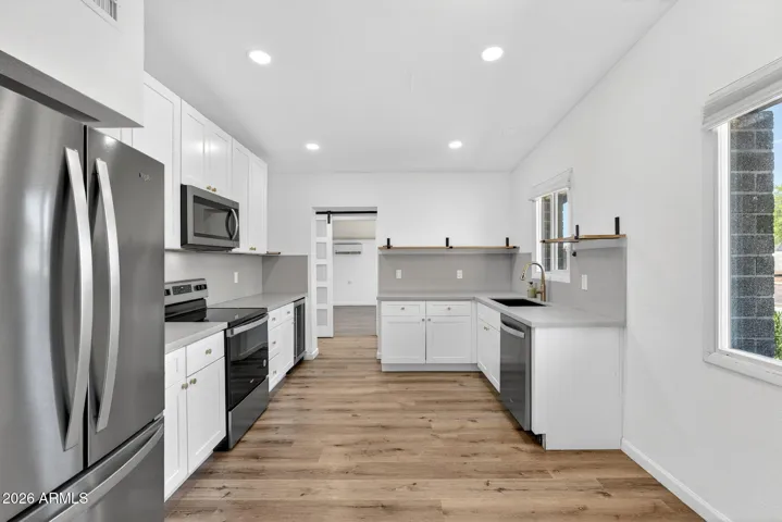 Spacious living room, neutral LVP flooring throughout, matte black fixtures, recessed lighting, stainless steel appliances.