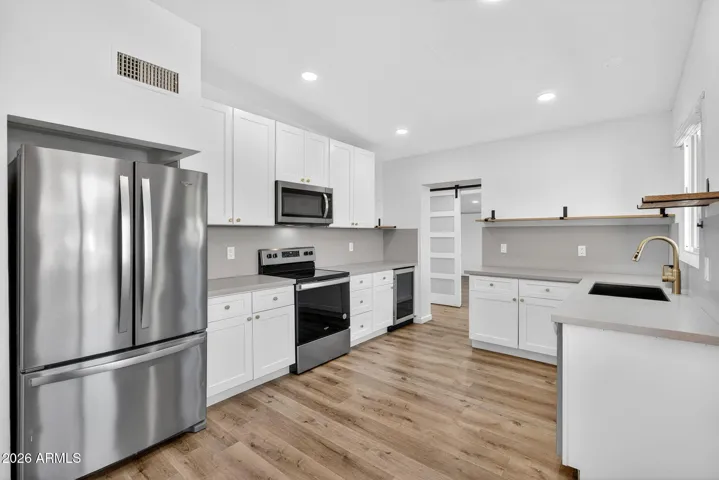 Spacious living room, neutral LVP flooring throughout, matte black fixtures, recessed lighting, stainless steel appliances.