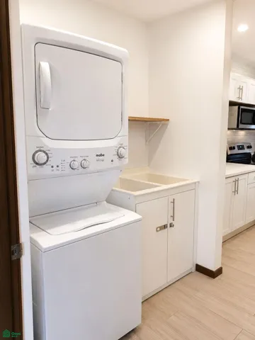 Stacked washer and dryer with an adjacent utility sink and storage.