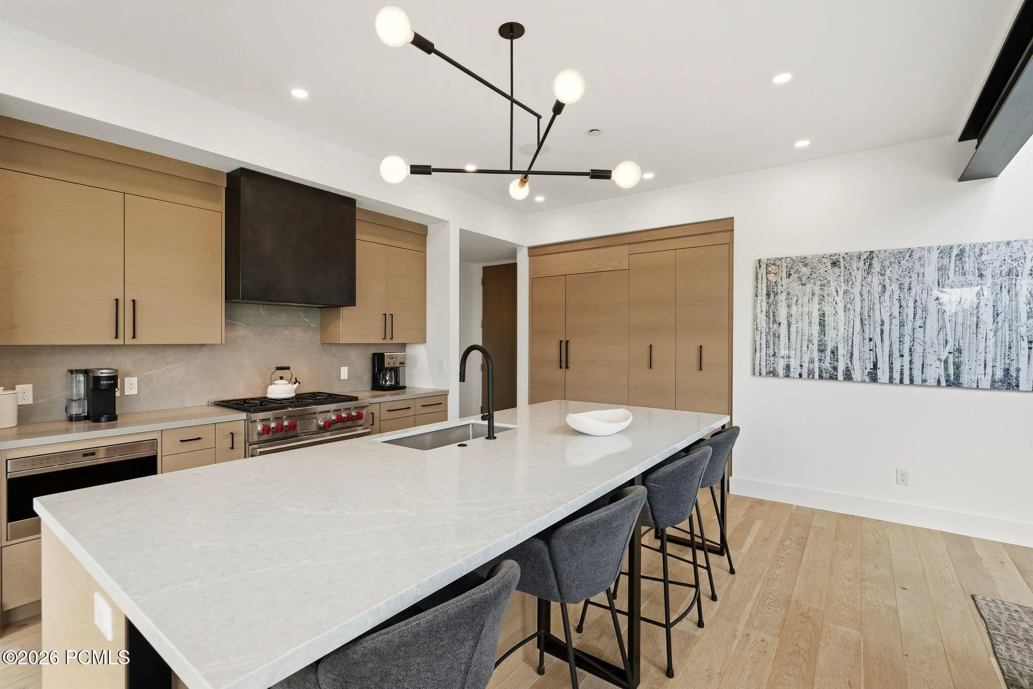 Gourmet kitchen featuring a substantial island with seating, a professional-grade range, custom light wood-finish cabinetry, a large built-in refrigerator, and light wood-finish flooring