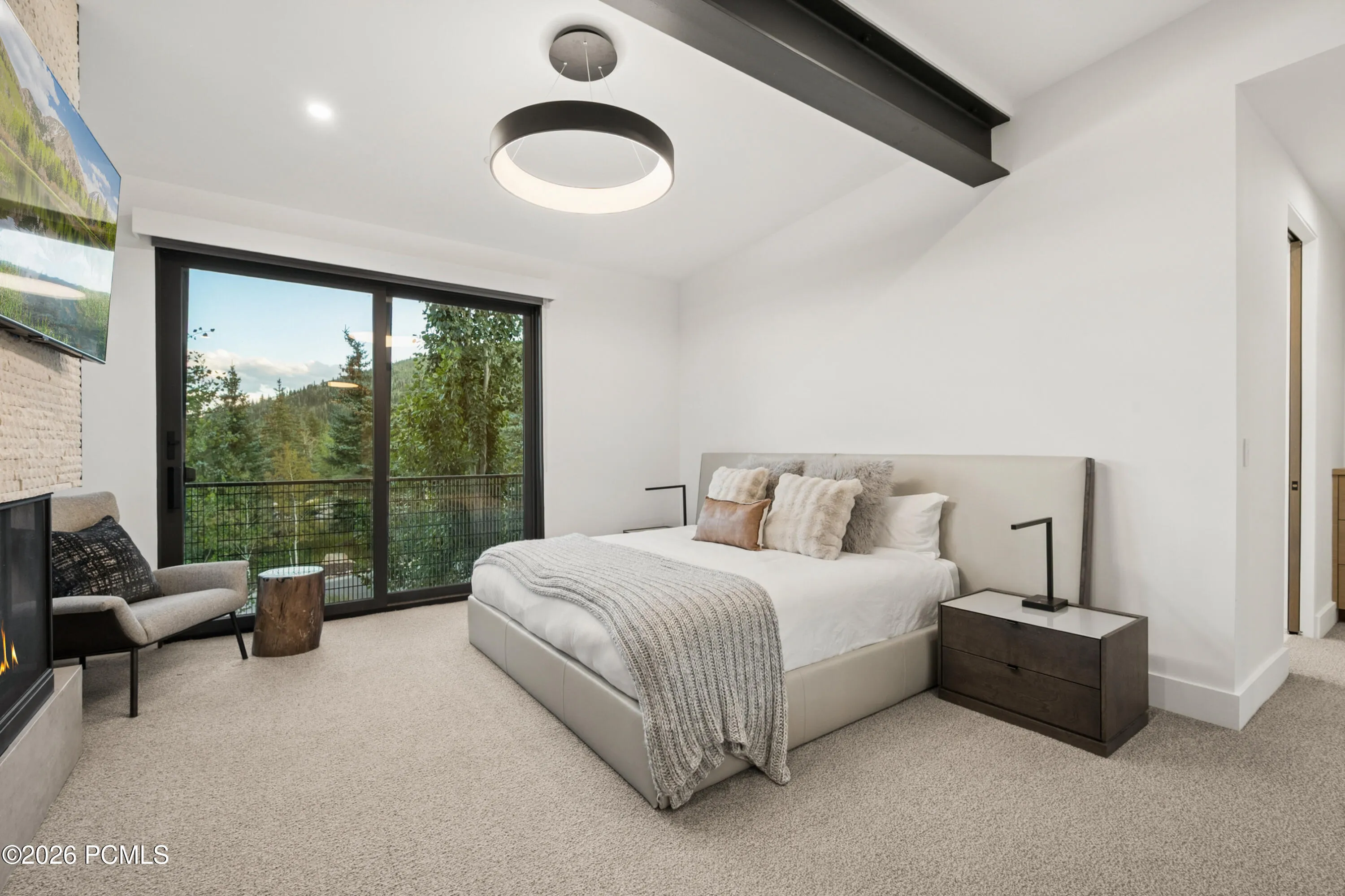 Spacious room featuring a floor-to-ceiling glass sliding door, leading to a private balcony with mountain and tree scenery