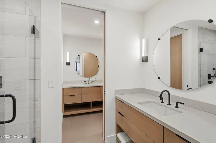 Contemporary bathroom featuring light wood-finish dual vanities with an integrated sink, matte black fixtures, and a large circular mirrors