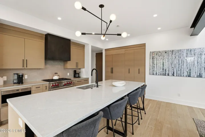 Gourmet kitchen featuring a substantial island with seating, a professional-grade range, custom light wood-finish cabinetry, a large built-in refrigerator, and light wood-finish flooring