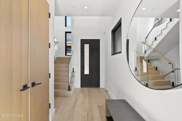 Entryway featuring wood-finish flooring, a contemporary staircase with glass railings and wood handrails, a solid core entry door with vertical glass insert.