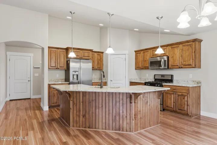 Gourmet kitchen featuring a central island with integrated sink, custom Alder cabinetry, stainless steel appliances, granite countertops, and hardwood flooring.