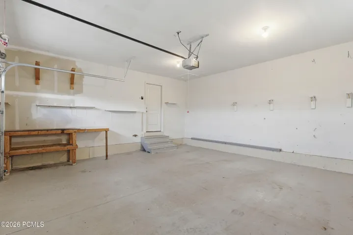 Spacious garage featuring a concrete floor, overhead lighting, 2 large windows and an automatic garage door opener