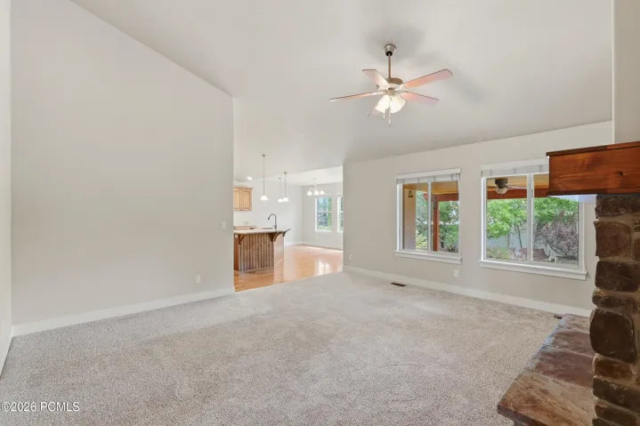 Bright family room with large windows, a stone fireplace, vaulted ceilings and a ceiling fan.