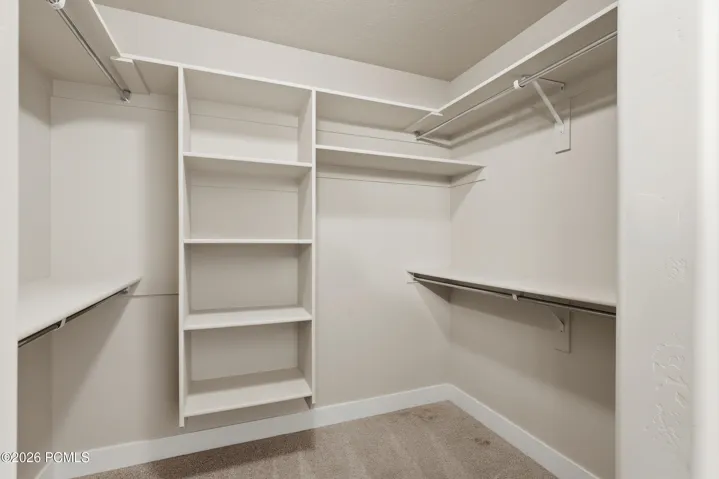 Spacious master suite walk-in closet featuring built-in shelving, multiple hanging rods, and neutral carpet flooring