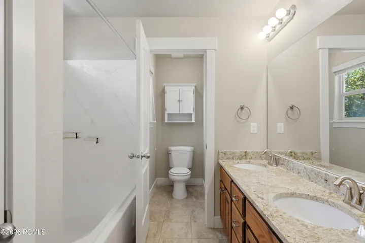 Master suite bathroom featuring a double vanity with stone countertops, undermount sinks, a large mirror, a large bath/shower and a window with natural light.