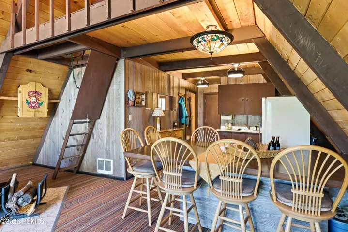A-frame cabin kitchen with dining bar stools, loft ladder, wood-burning stove chimney, and open layout in Timberlake, Utah