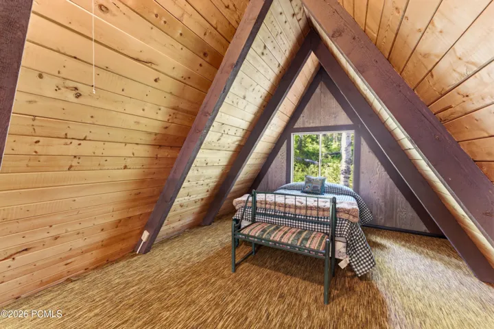 Cozy A-frame cabin loft with vaulted wood ceiling, small window, and charming rustic decor in Timberlake, Utah