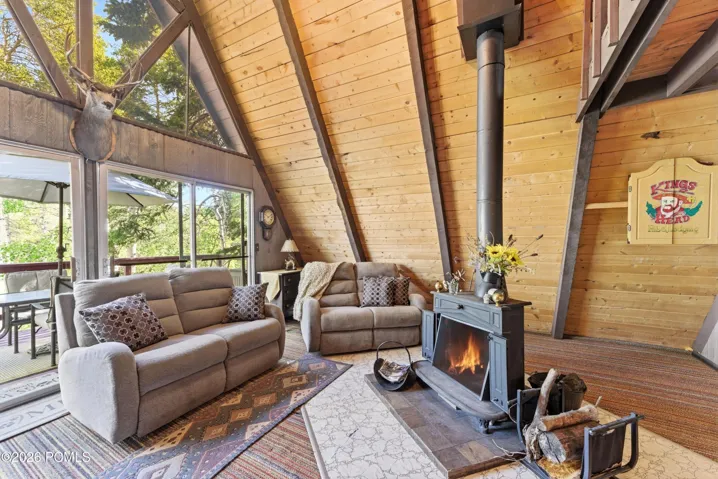 Cozy A-frame cabin living room with lit wood-burning stove, comfortable sofas, vaulted pine ceiling, and large windows in Timberlake, Utah