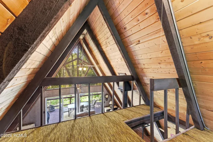 A-frame cabin loft landing with exposed wood beams, triangle window, and open view to main floor below in Timberlake, Utah