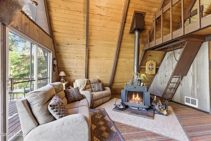 A-frame cabin living room with crackling wood stove fireplace, cozy sofas, loft ladder, and rustic cabin charm in Timberlake, Utah