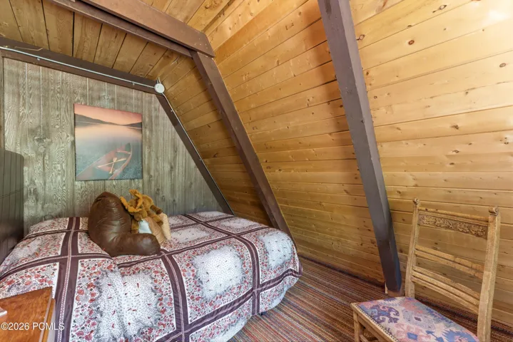 Loft bedroom in A-frame cabin with vaulted wood ceiling, cozy quilt bed, and rustic mountain decor in Timberlake, Utah