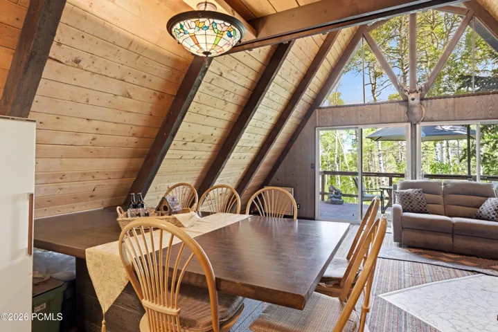 A-frame cabin dining area with vaulted wood ceiling, Tiffany pendant light, and sliding glass door to living room in Timberlake, Utah