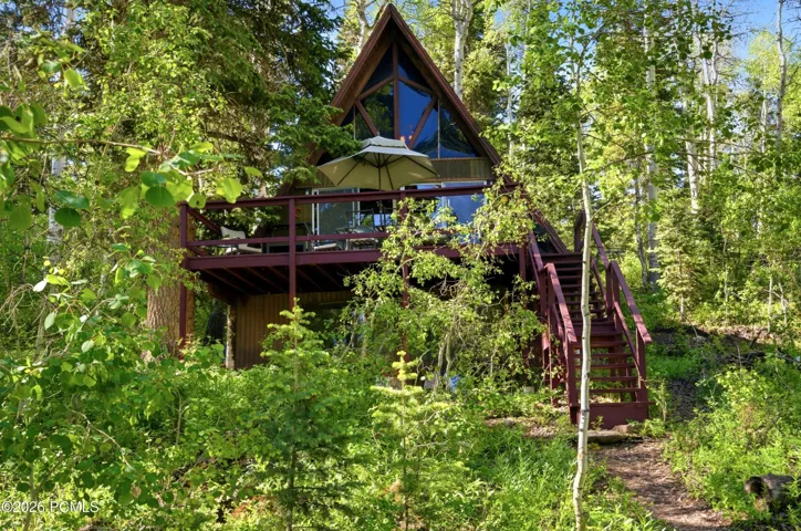 A-frame cabin with wraparound deck and patio umbrella nestled among tall trees in Timberlake, Utah
