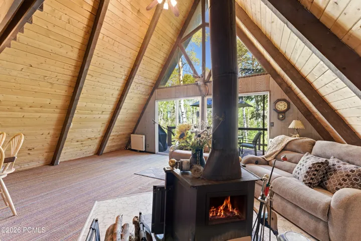 Bright A-frame cabin living room with wood-burning stove, vaulted pine ceiling, large windows, and natural light in Timberlake, Utah