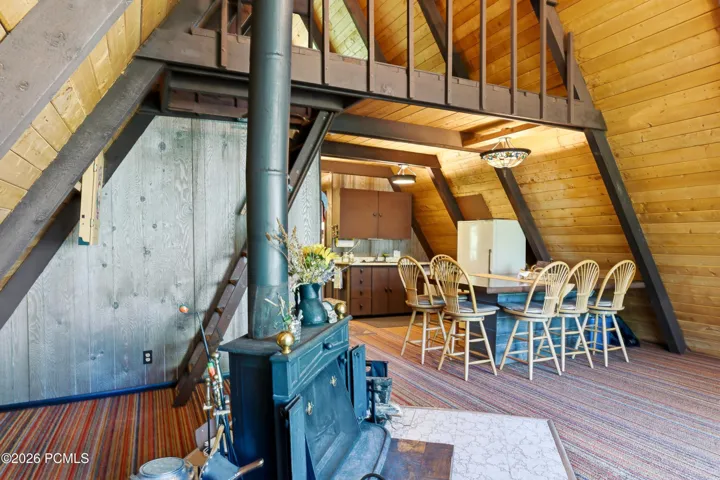Open-plan A-frame cabin interior showing wood-burning stove, dining area with bar stools, and loft ladder in Timberlake, Utah