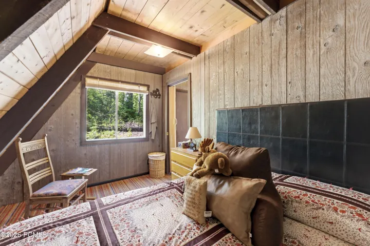 Bedroom with sloped A-frame ceiling, window to forest, bed, and wood accent wall in Timberlake, Utah