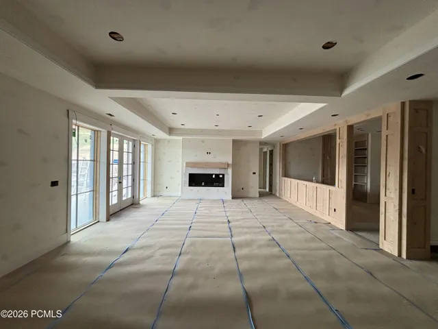 Spacious basement living space featuring a fireplace, tray ceiling, and French doors