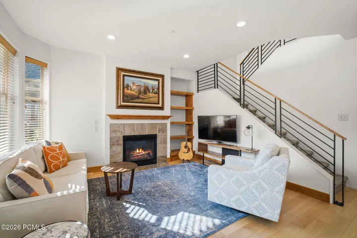 Bright, open great room with gas fireplace, hardwood floors, and soaring staircase to loft/office — Park City townhome with upgraded lighting and move-in ready finishes.