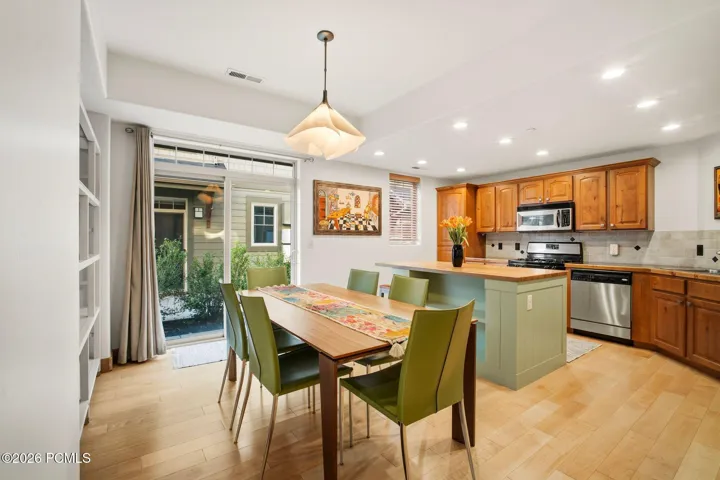 Open-concept kitchen and dining area with sliding glass door, pendant lighting, and green chairs — ideal for entertaining in this Park City townhome near Redstone 8 Cinemas.