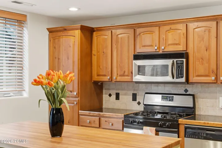 Kitchen detail with stainless gas range, over-range microwave, and custom tile backsplash — quality appliances and wood cabinetry in this Park City townhome at Fox Point at Redstone.