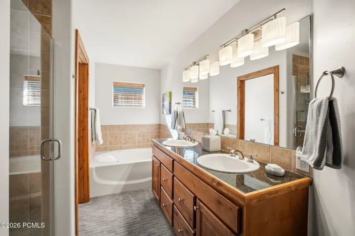 Primary en-suite bathroom with double vanity sinks, jetted soaking tub, separate shower, and wood cabinetry — luxurious primary bath in this Park City townhome.