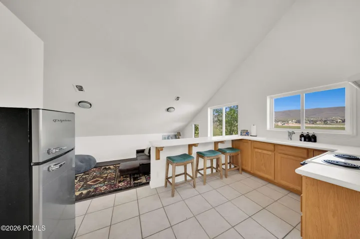 Kitchenette featuring a white tiled floor, wood-finish cabinetry, a white countertop with an integrated sink, a built-in electric cooktop, and a retro-style refrigerator