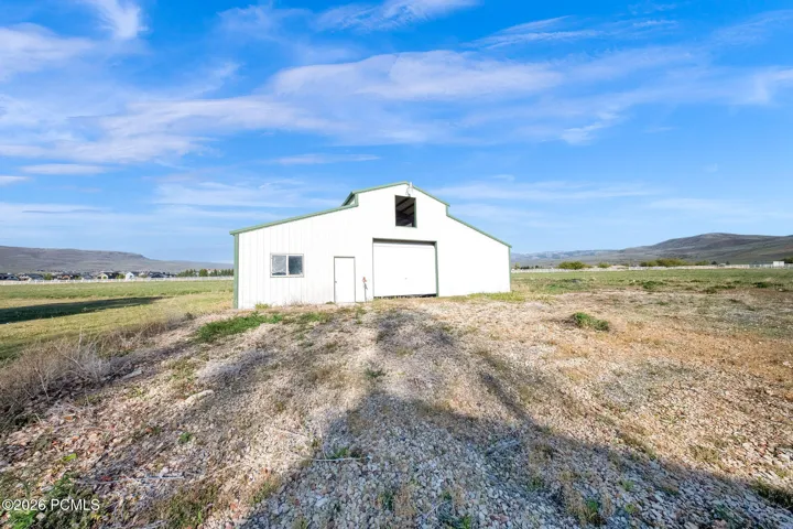 White metal barn with green trim, featuring a large roll-up door, an entry door, and a window