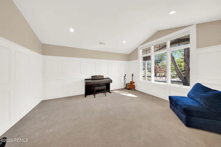 Spacious room featuring vaulted ceilings, recessed lighting, expansive window wall, light-colored carpeting, and wainscoting