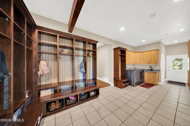Spacious mudroom featuring extensive built-in wooden cabinetry with individual cubbies and hooks, an integrated bench, and tiled flooring