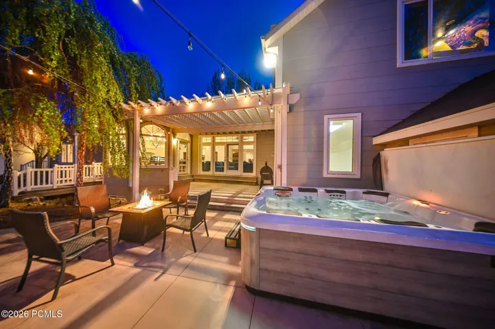 Spacious concrete patio featuring a built-in hot tub, fire pit, and string lighting
